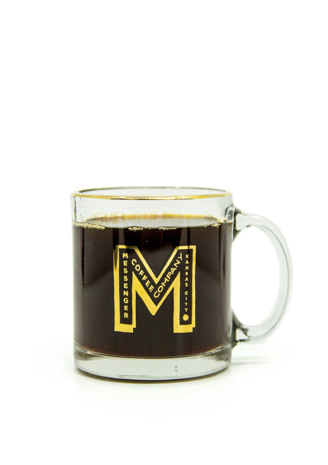Gold M Logo Glass Mug filled with dark coffee, featuring elegant gold M design and rim, transparent glass with handle